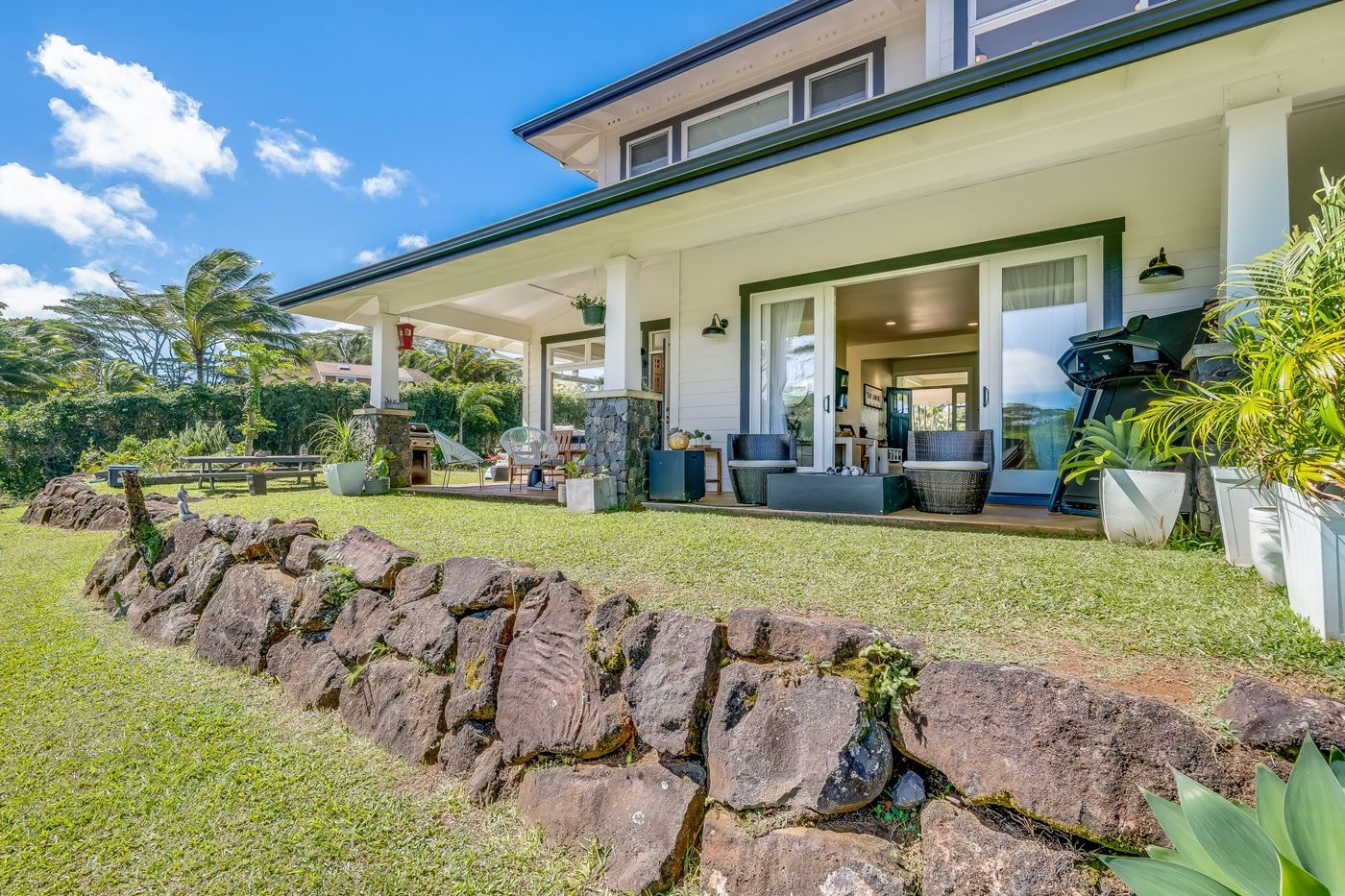 The back of the house with a covered lanai, lava rock wall and lawn