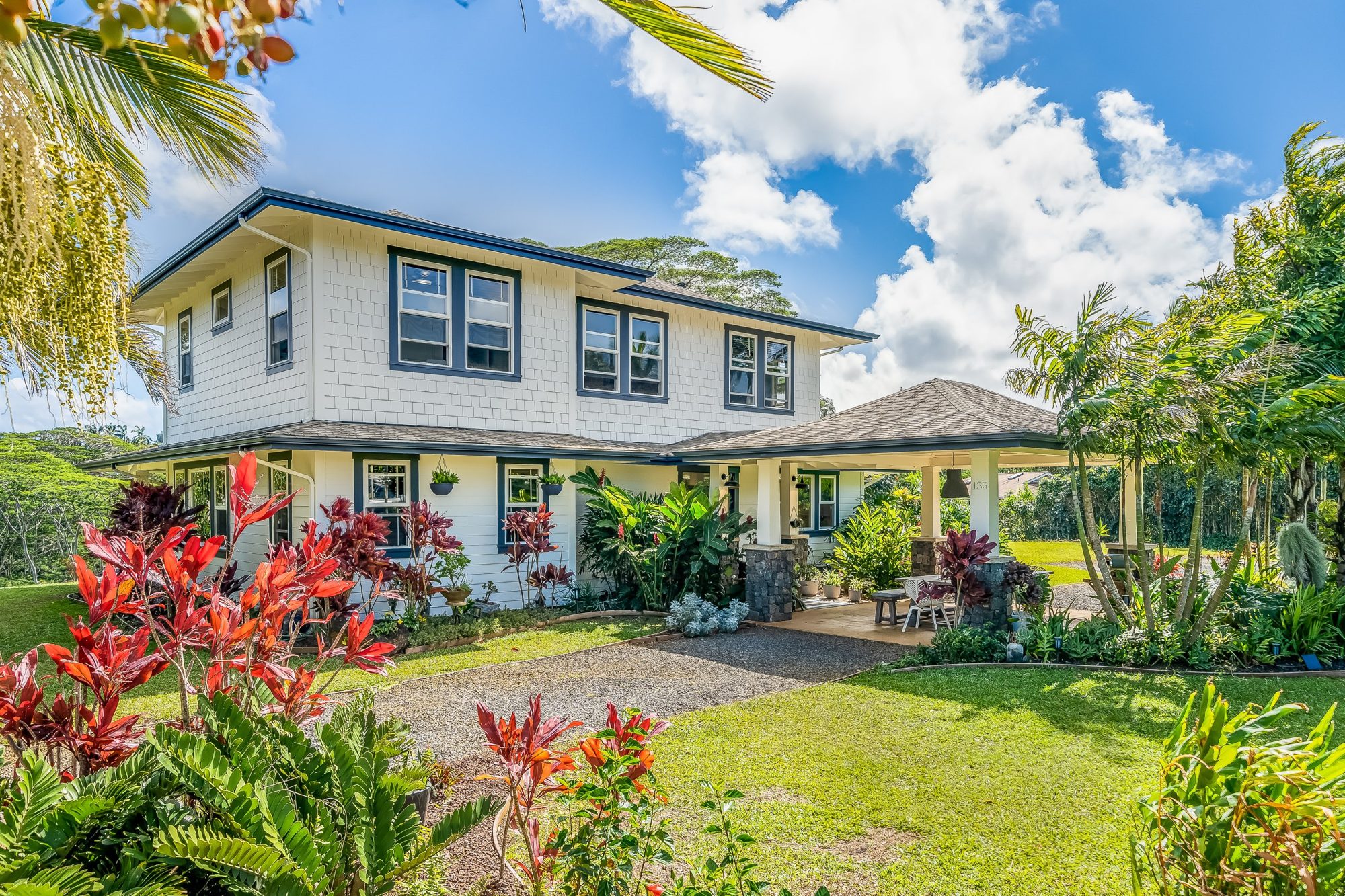 The white two-story house with blue trim, red ti plants and a green lawn